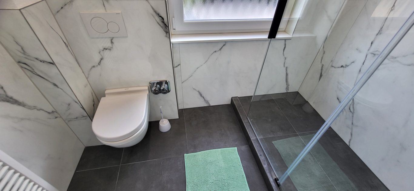 Moderne Badezimmeransicht mit Dusche, Toilette und grauem Bodenbelag. Moderne Badezimmeransicht mit Dusche, Toilette und grauem Bodenbelag.