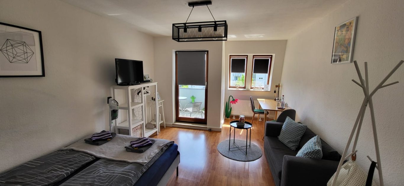 Heller, moderner Wohnraum mit Bett, Sofa, Tisch, TV und großen Fenstern Heller, moderner Wohnraum mit Sofa, Tisch, TV und großen Fenstern.