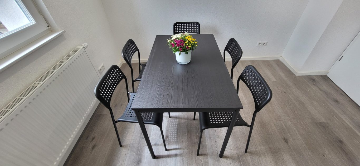 Ein rechteckiger Esstisch mit fünf Stühlen und einer Blumenvase in der Mitte. Ein rechteckiger Esstisch mit fünf Stühlen und einer Blumenvase in der Mitte.