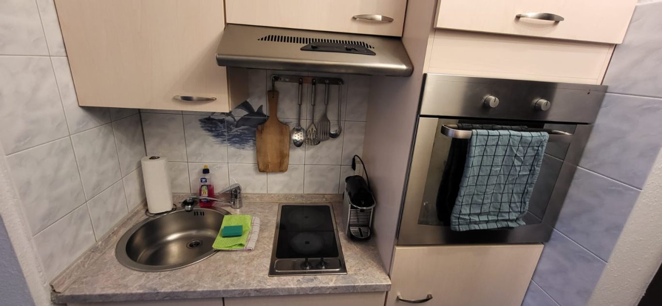 Kleine moderne Küche mit Spüle, Kochfeld und Ofen. Kleine moderne Küche mit Spüle, Kochfeld und Ofen. Handtuch hängt am Ofen.