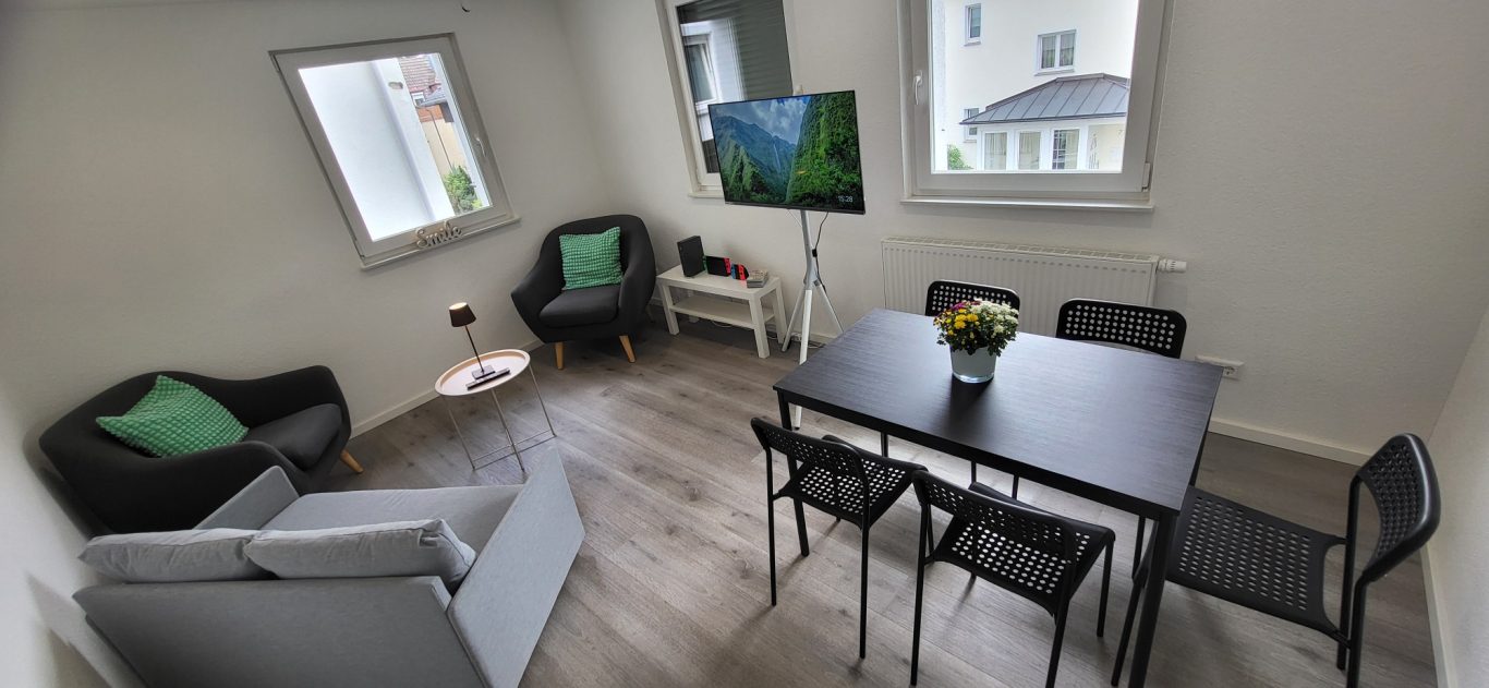 Helles Zimmer mit Sofa, Tisch, Stühlen und Fernseher, grüne Kissen auf den Stühlen. Helles Zimmer mit Sofa, Tisch, Stühlen und Fernseher, grüne Kissen auf den Stühlen.