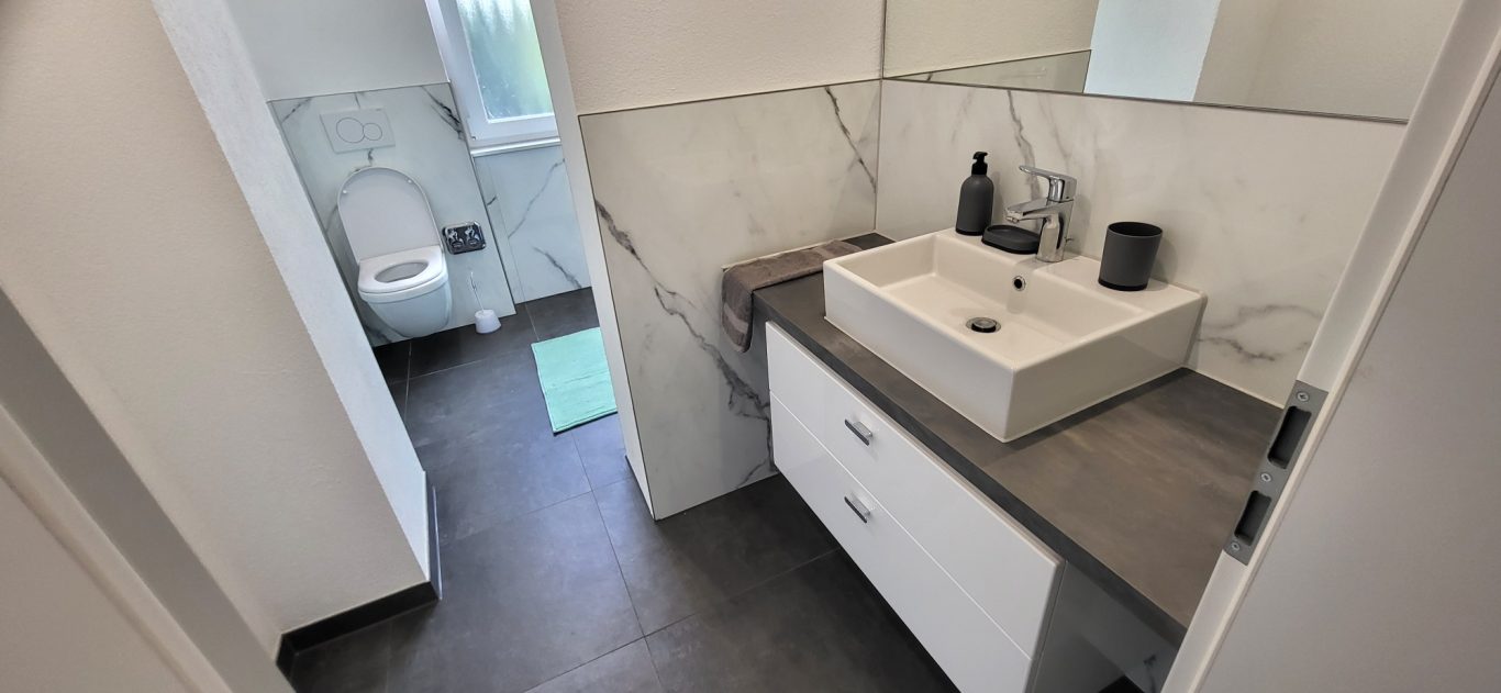 Moderne Badezimmeransicht mit Waschbecken, Toilette und eleganten Fliesen. Moderne Badezimmeransicht mit Waschbecken, Toilette und eleganten Fliesen.